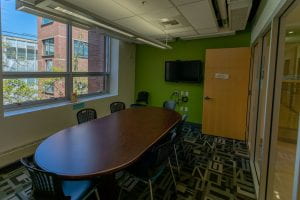 Small meeting room with round table, a couple chairs and a wall-mounted TV.