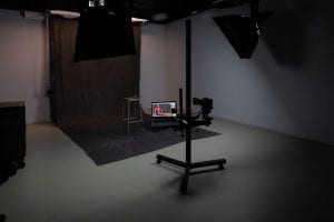A picture of the production studio with a black backdrop for portraits set up, a stool, camera and laptop.
